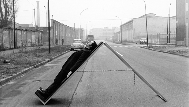 Foto in bianco e nero di una strada cittadina a due corsie con un uomo adagiato su un supporto diagonale.